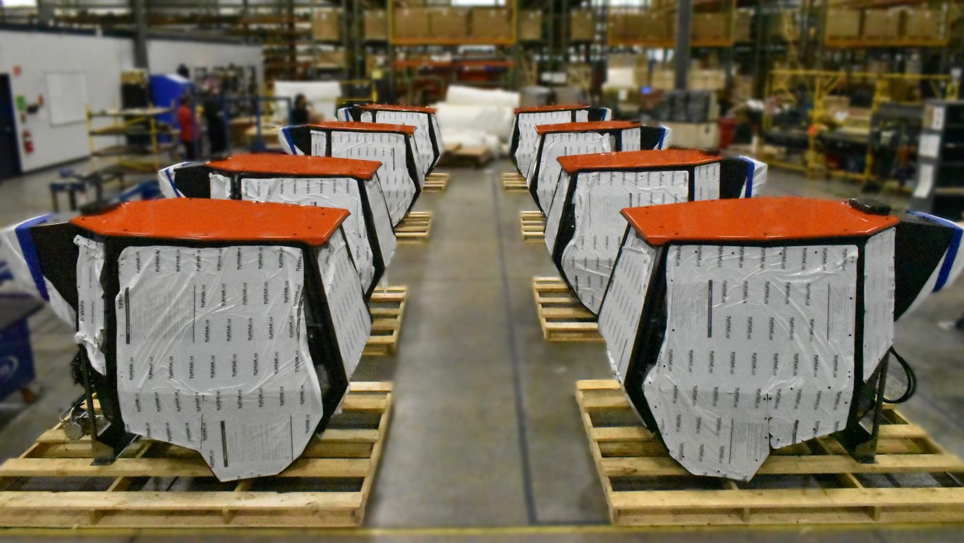 Cab Assembly Rows of manufactured vehicle operator cabs sitting on wooden pallets inside a spacious factory warehouse