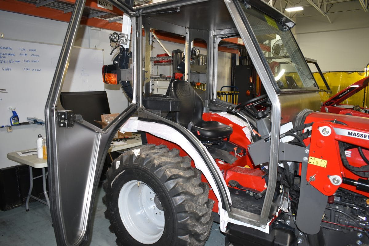 Curtis Industries Interior view of a compact red tractor with an enclosed metal cab, open door, and large rear tire
