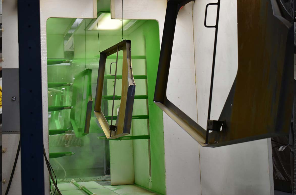 An industrial electrostatic powder coating booth where metal vehicle door frames hang from an overhead conveyor line.