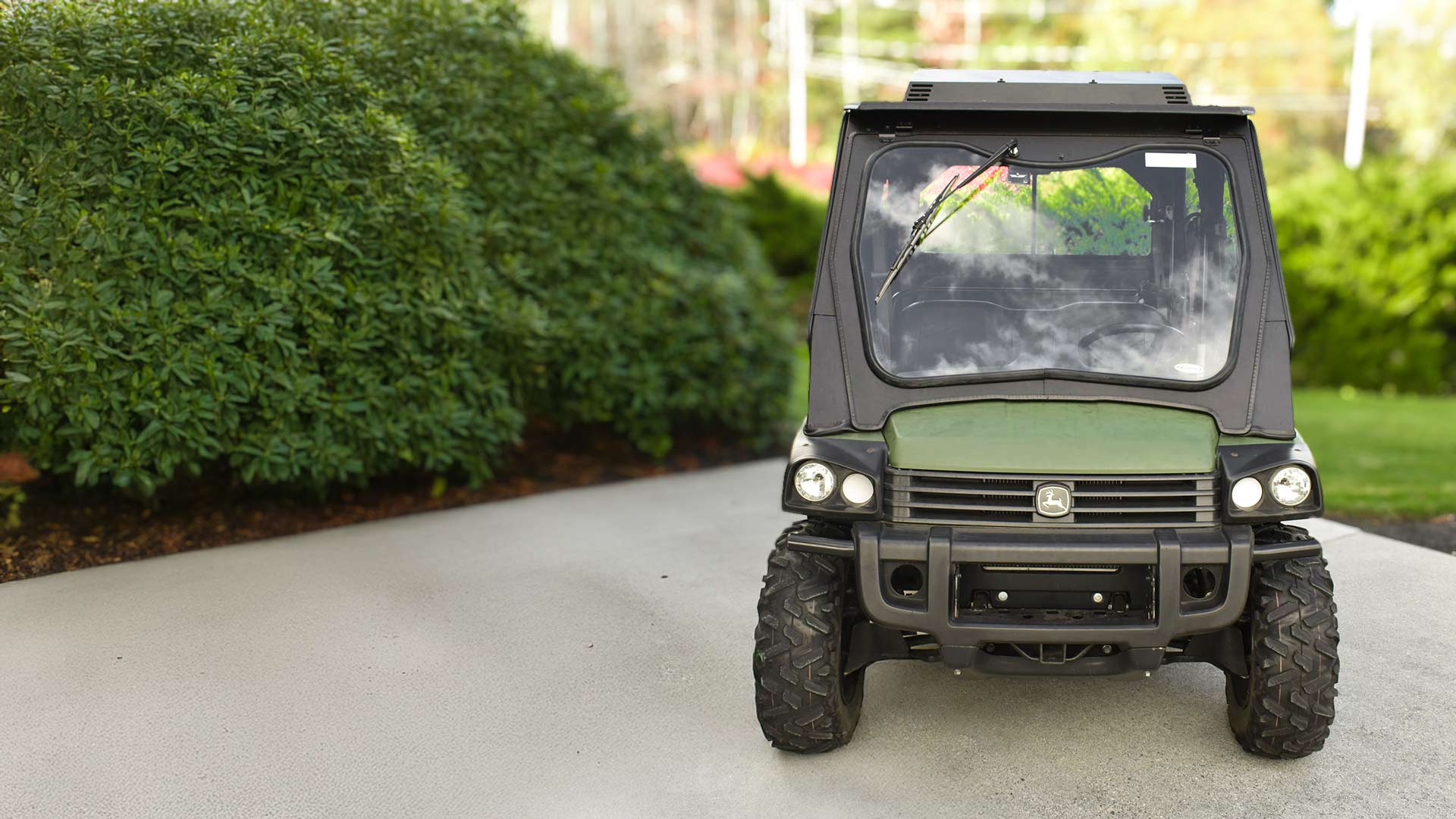John Deere Gator UTV with cab enclosure in front of green foliage